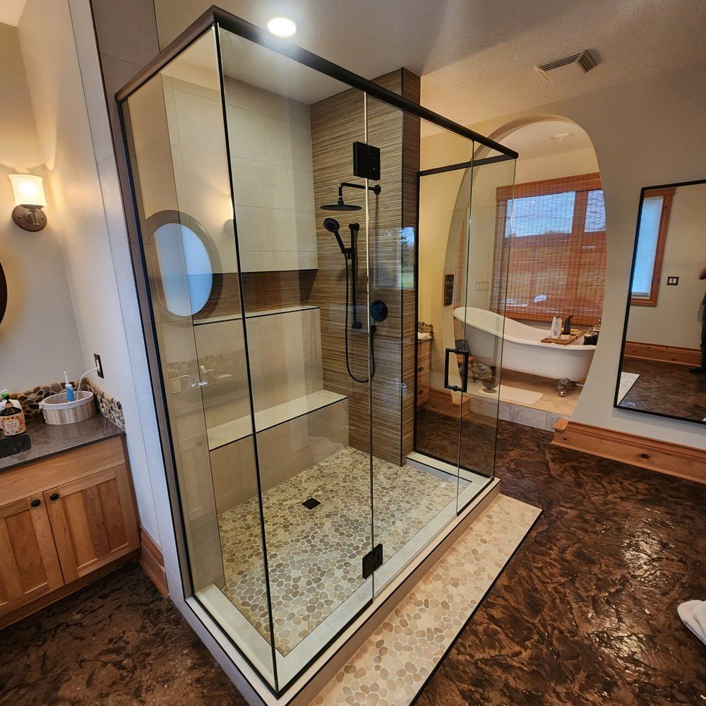 Modern glass shower enclosure with pebble floor in a Sherwood Park bathroom by XMP Construction.