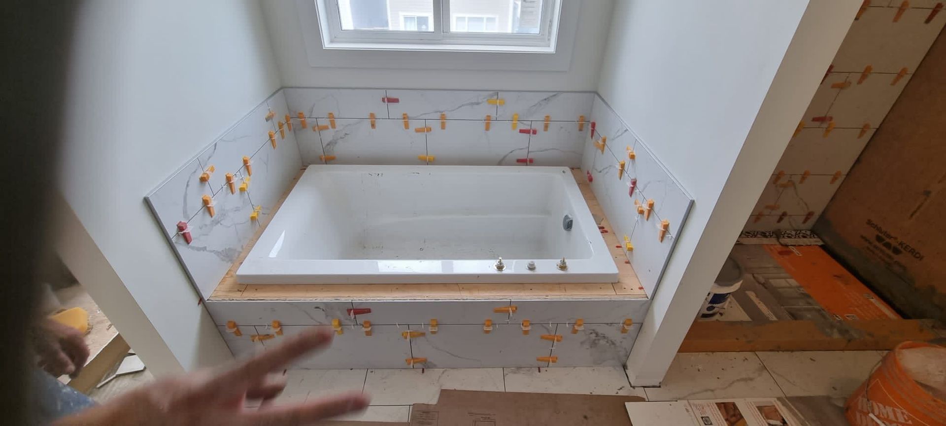 Installation of elegant white marble-look tiles around a soaker tub in a Sherwood Park bathroom by XMP Construction.