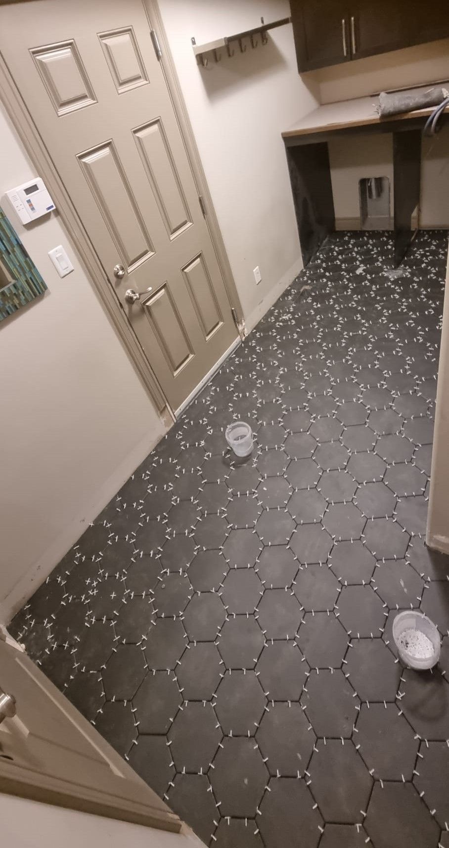 Installation of dark grey hexagon floor tiles in a Sherwood Park laundry room by XMP Construction.