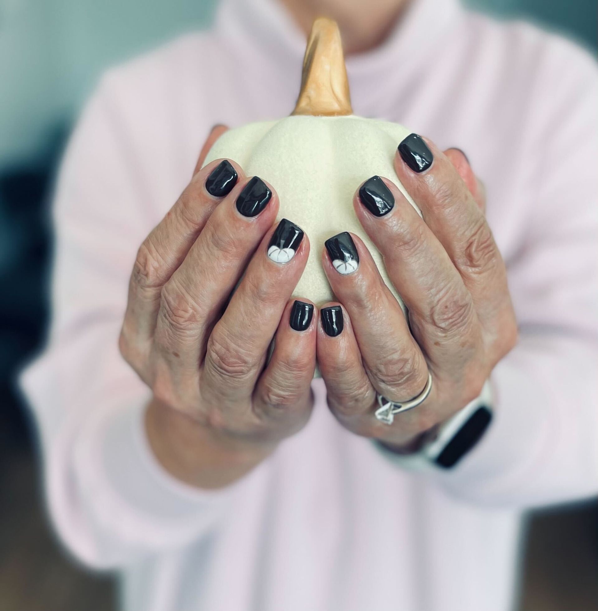 a woman with black nails is holding a white pumpkin