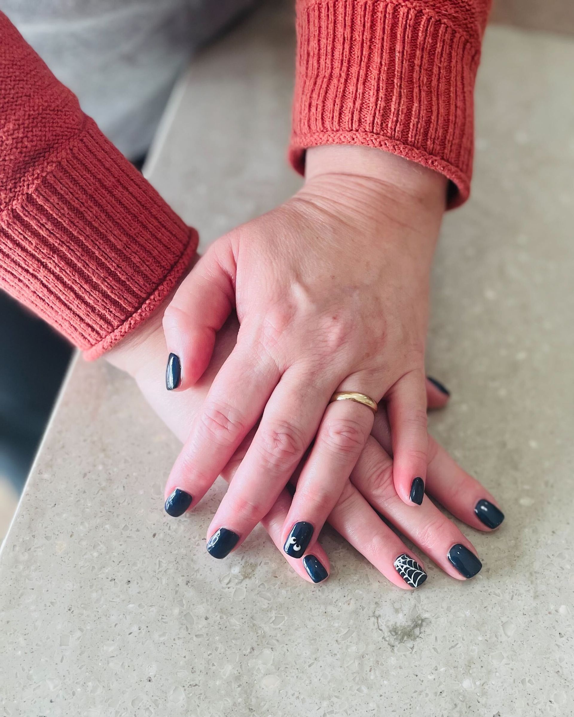 a woman 's hands with black nails and a gold ring