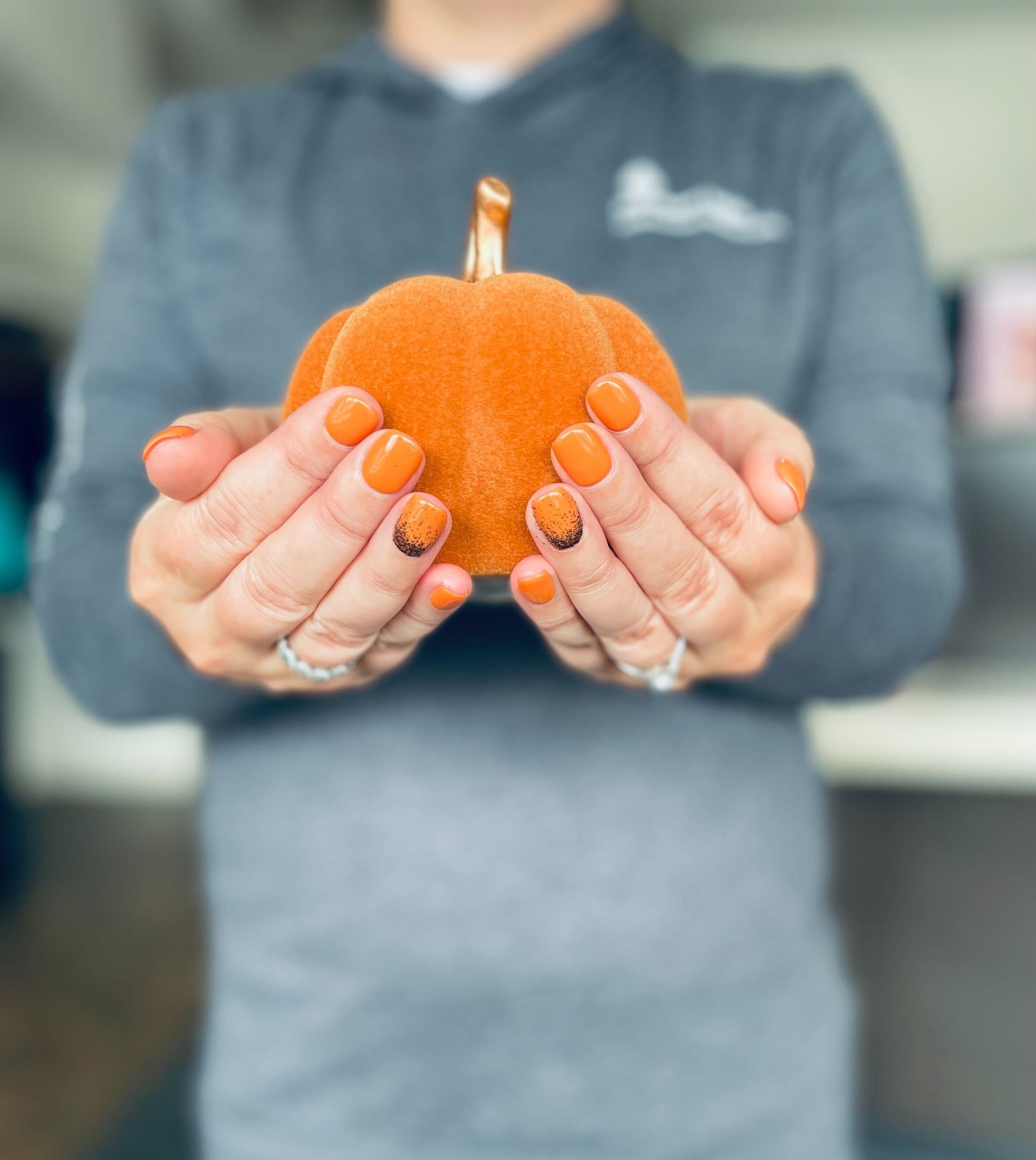 a woman with orange nails is holding a small pumpkin