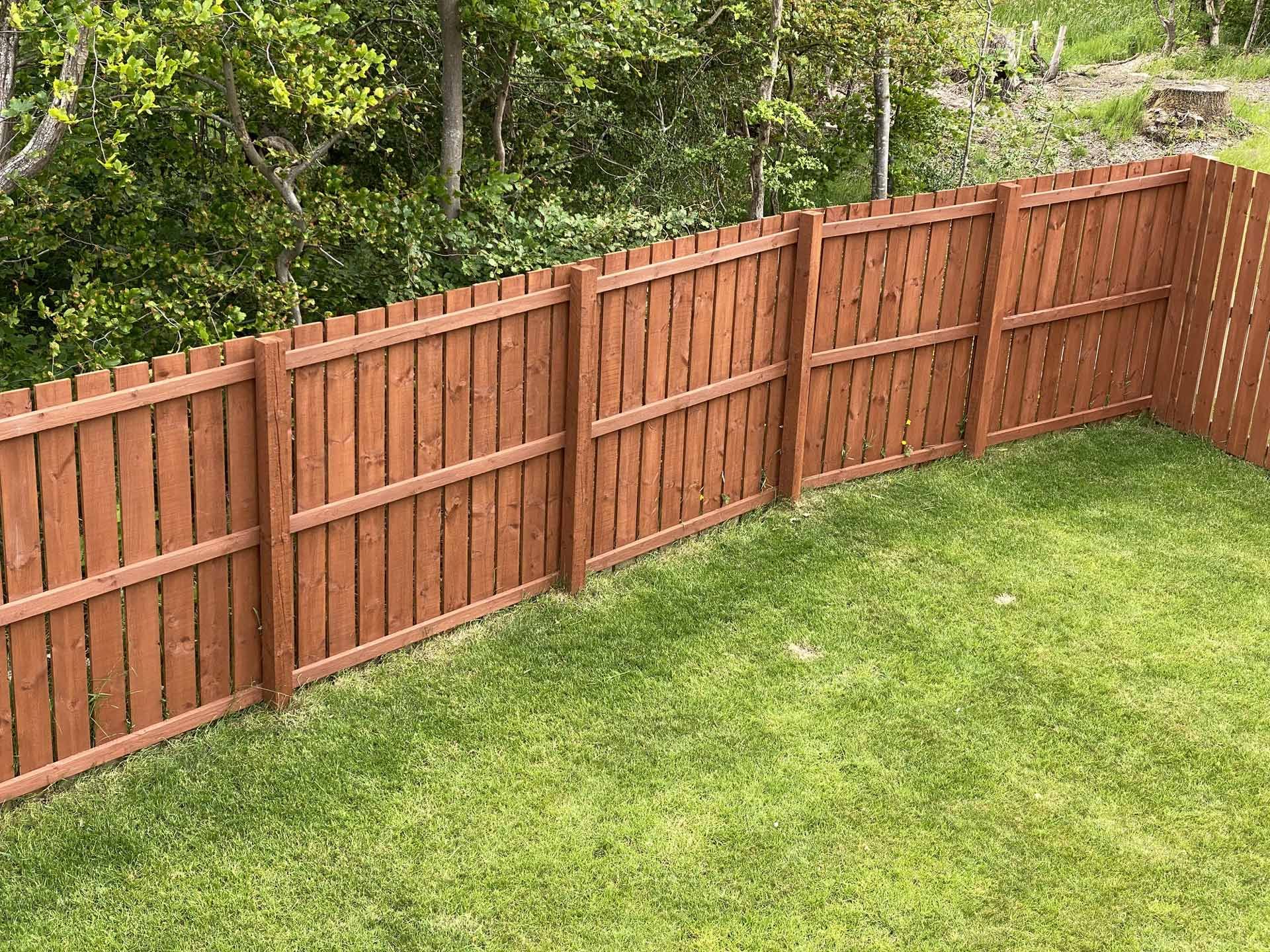 A wooden fence surrounds a lush green lawn in a backyard.