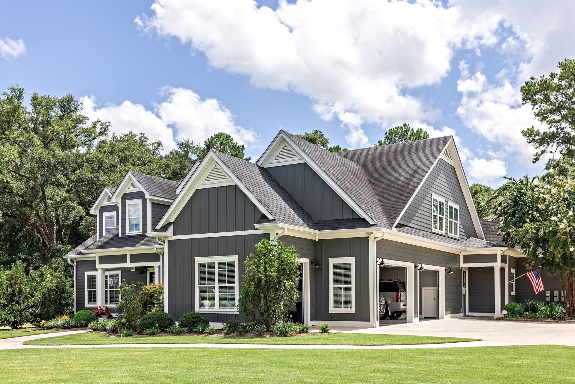 A large gray house with a black roof is sitting on top of a lush green field.