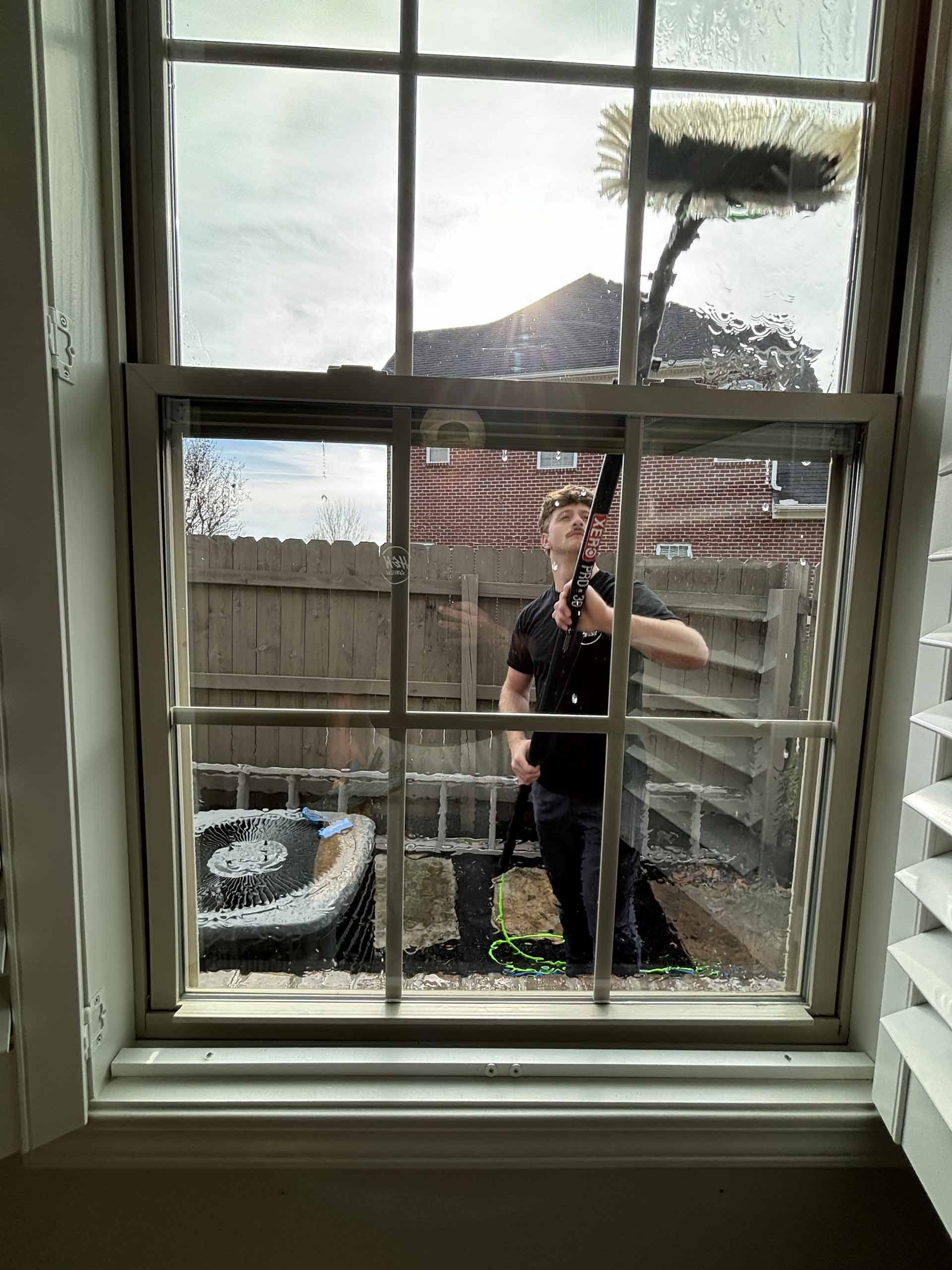 A man is cleaning a window with a broom.