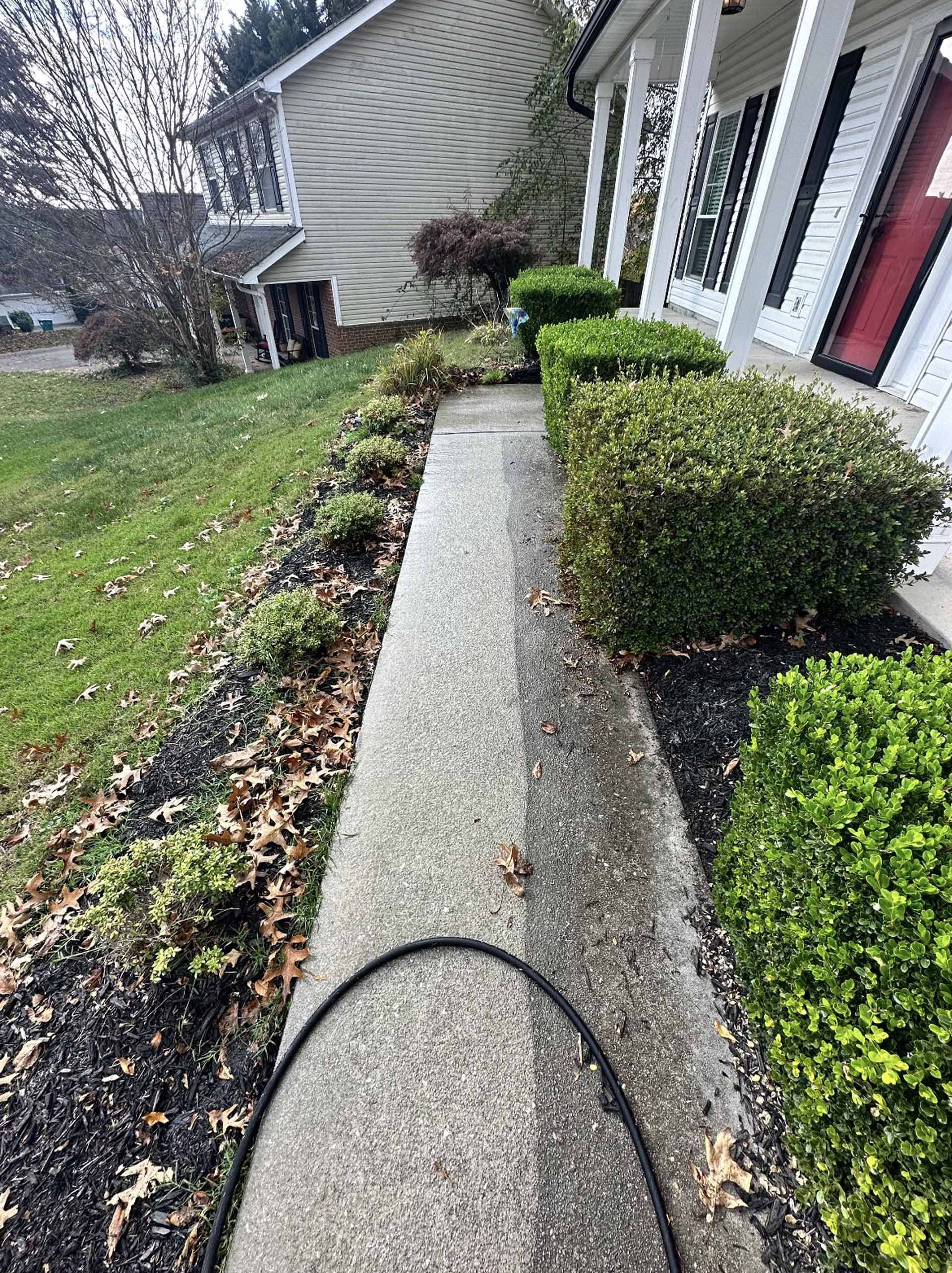 A sidewalk in front of a house with a hose attached to it.