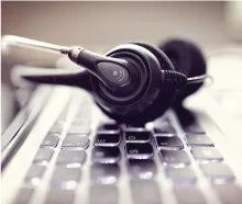 Auriculares apoyados sobre un teclado de ordenador portátil; auriculares negros, micrófono plateado.