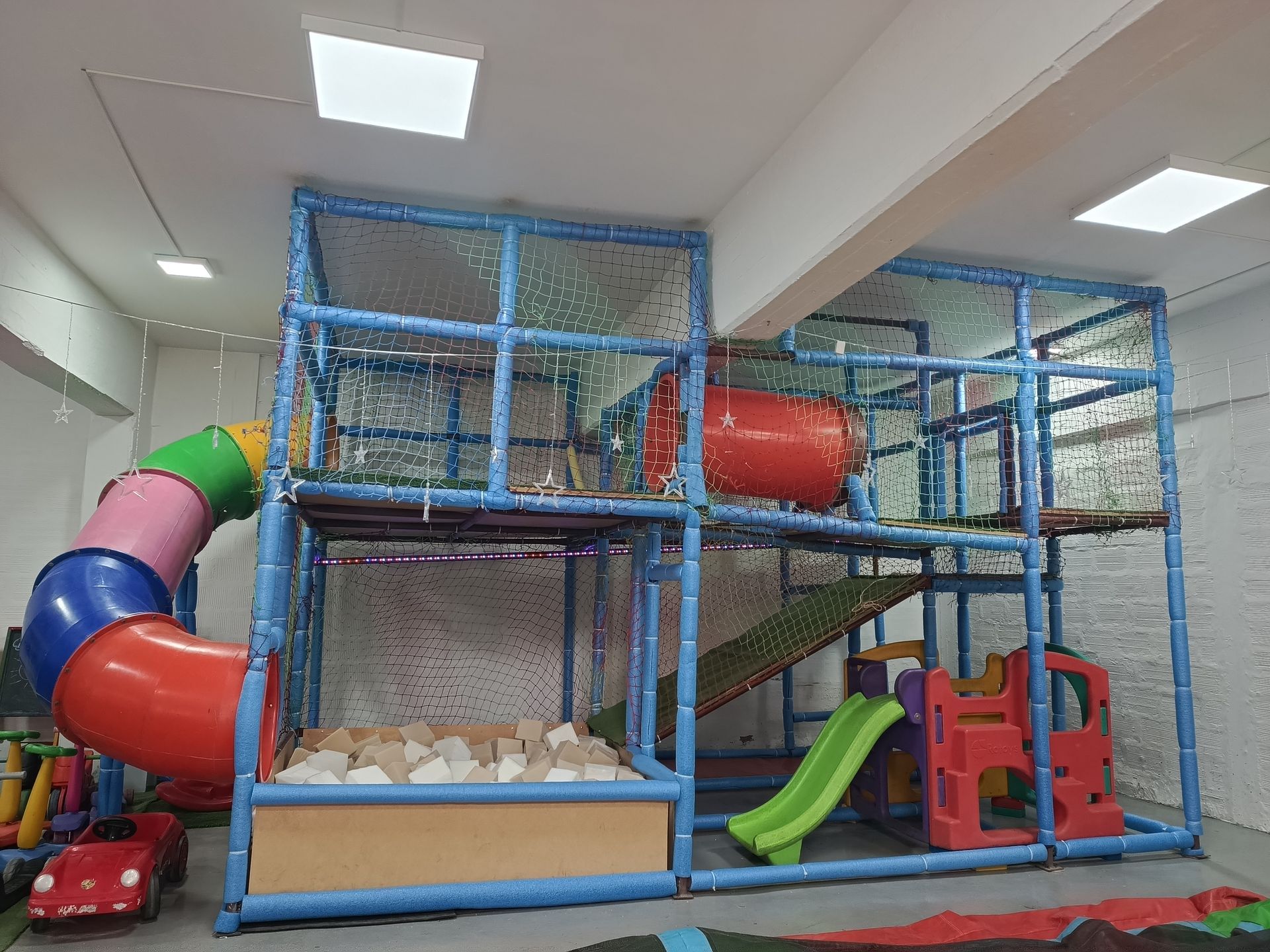 Área de juegos infantiles en el interior con un tobogán colorido, una estructura para escalar, un foso de pelotas
