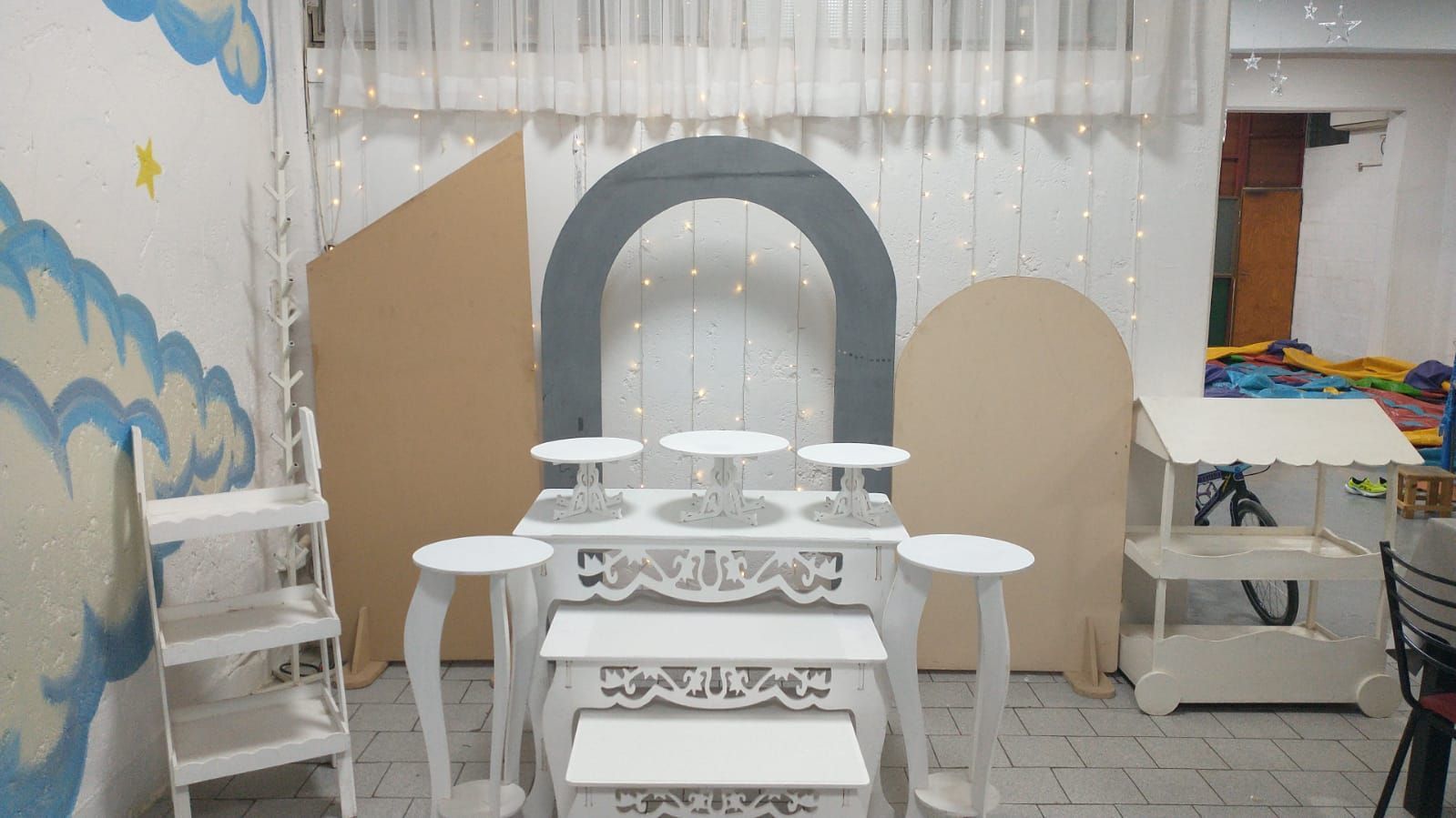 Fondo para evento con decoraciones en blanco y beige, soportes para pasteles y un arco.