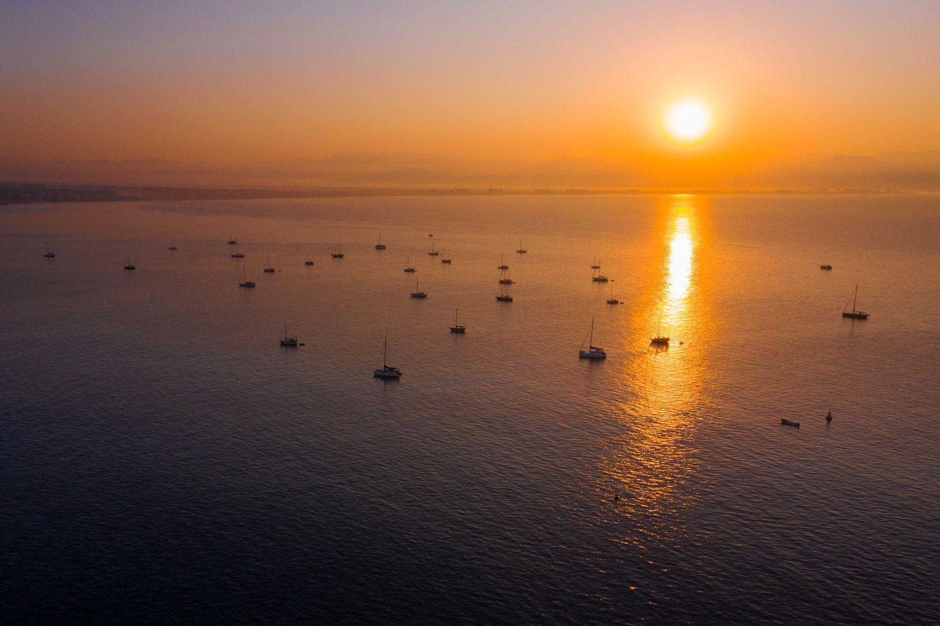 a group of boats are floating on top of a body of water at sunset .