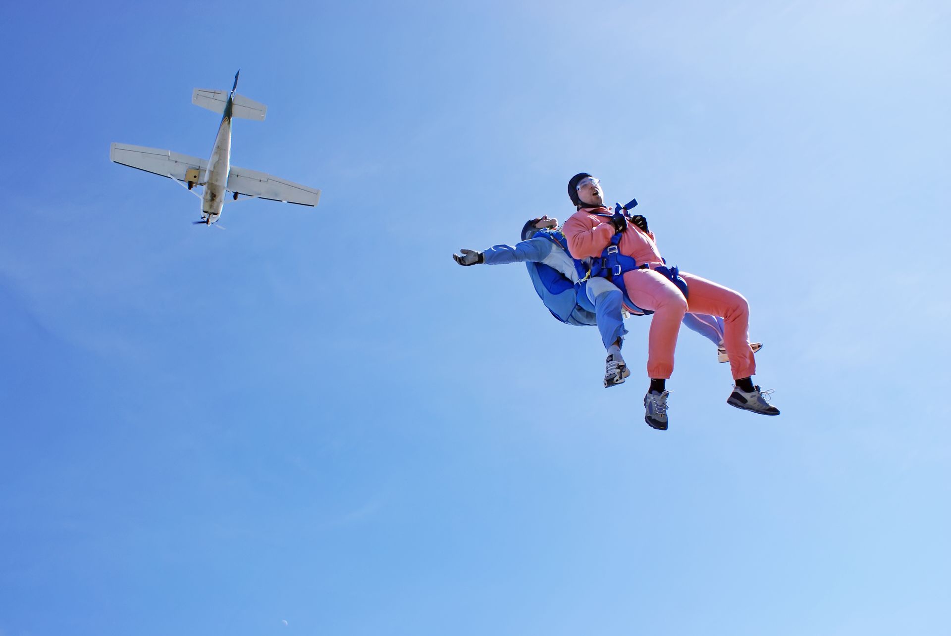 two people are flying through the air with a small plane flying in the background .