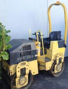 A yellow and black road roller is parked in front of a building.