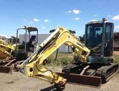 A yellow excavator is parked in a parking lot next to another excavator.