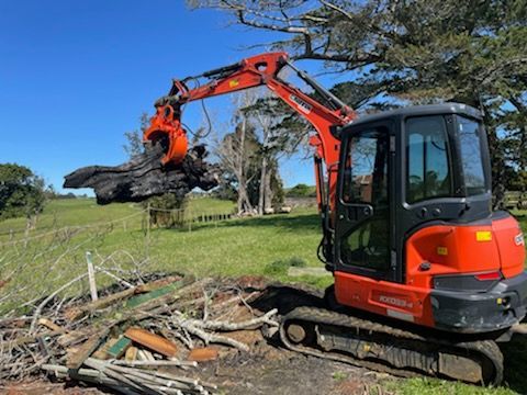 A red and black excavator is carrying a large log in a field.