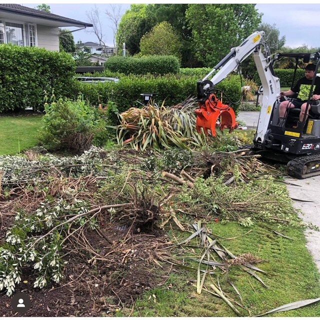 A man is driving a small excavator in a yard.