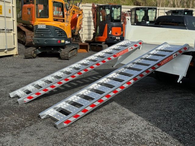 A pair of aluminum ramps are attached to the back of a truck