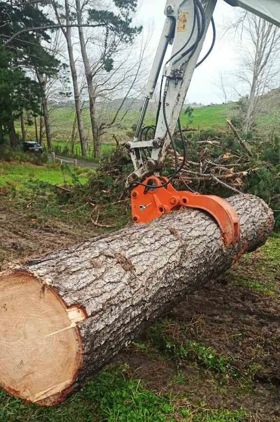 A large log is being lifted by a crane in a field.