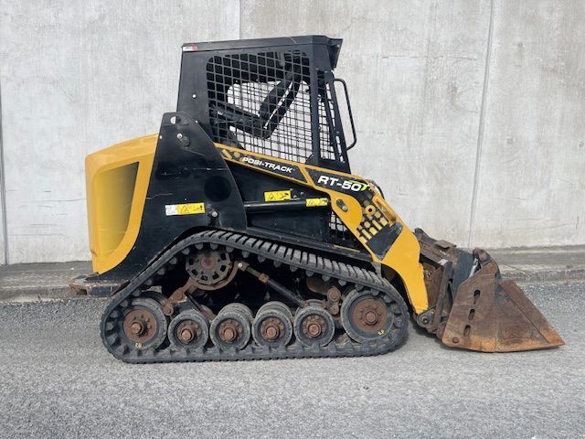 A yellow and black tracked bulldozer is parked in front of a concrete wall.