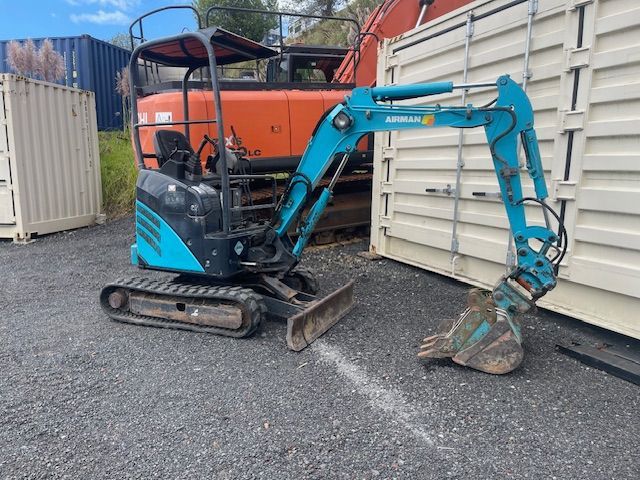 A small blue excavator is parked next to a white container.