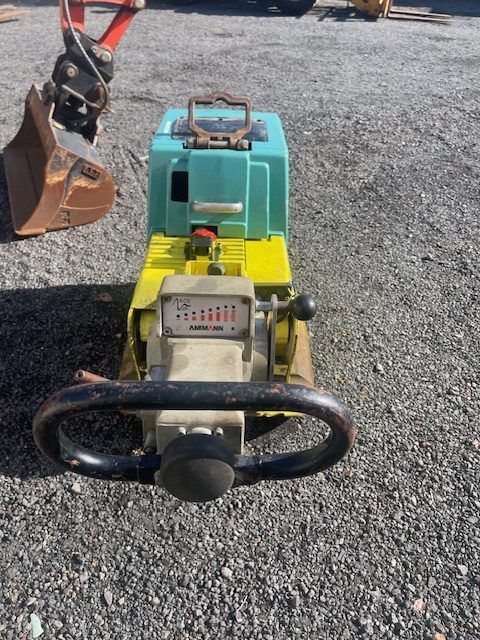 A yellow and green machine with a steering wheel is sitting on a gravel road