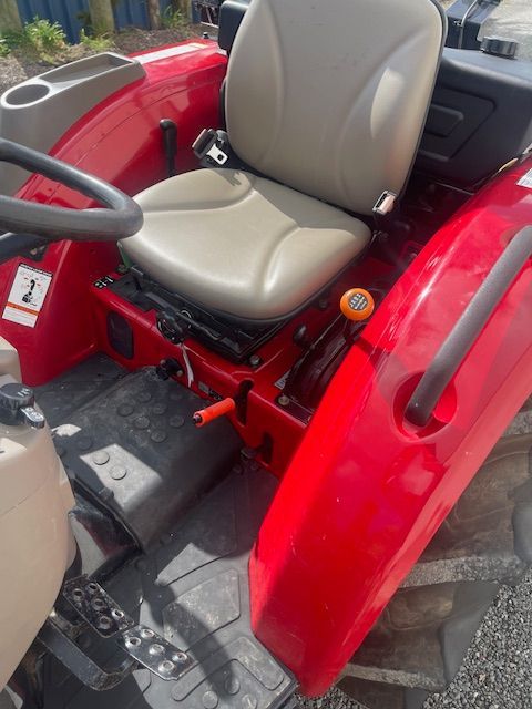 The inside of a red tractor with a tan seat and steering wheel.