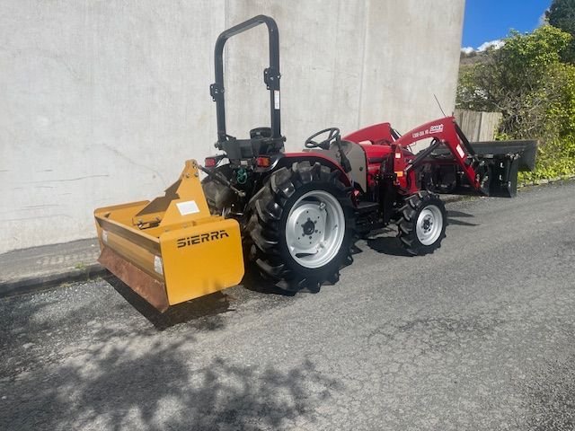 A red tractor with a yellow plow attached to it is parked on the side of the road.