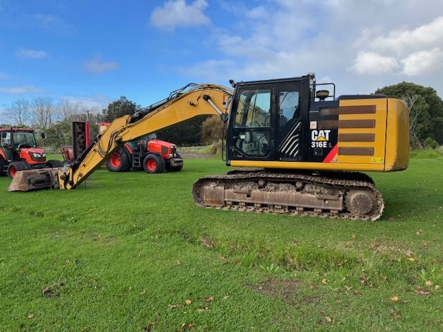 A cat excavator is parked in a grassy field next to a tractor.