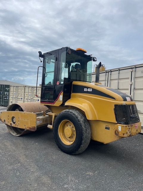 A yellow and black cat roller is parked in a parking lot