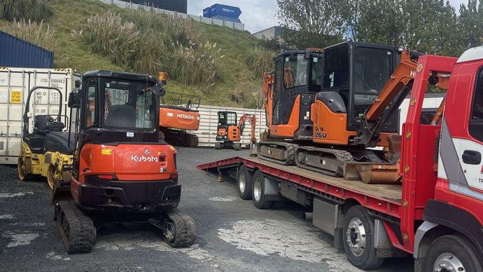 A red tow truck is carrying a bunch of construction vehicles.