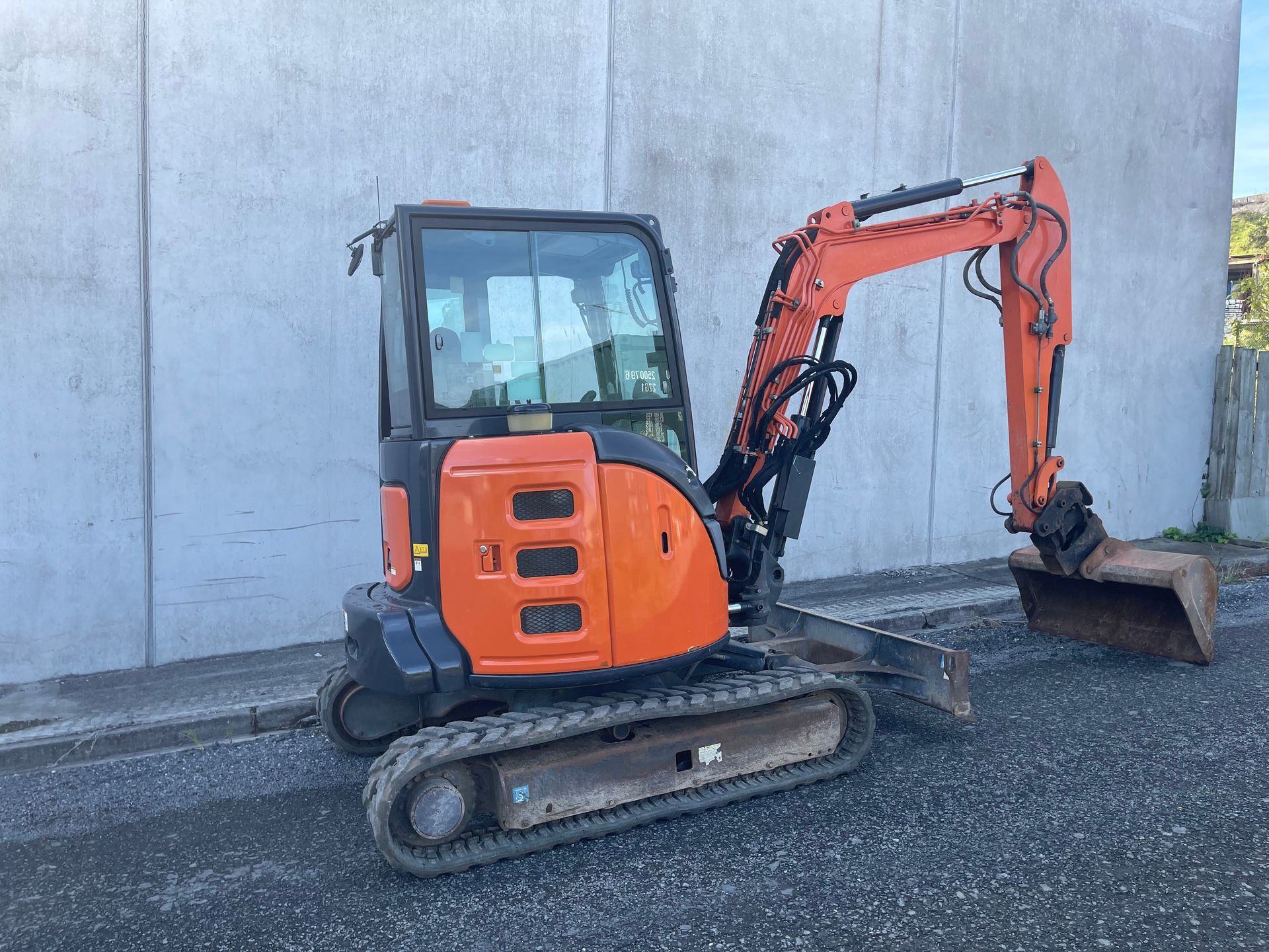A small orange excavator is parked in front of a concrete wall.
