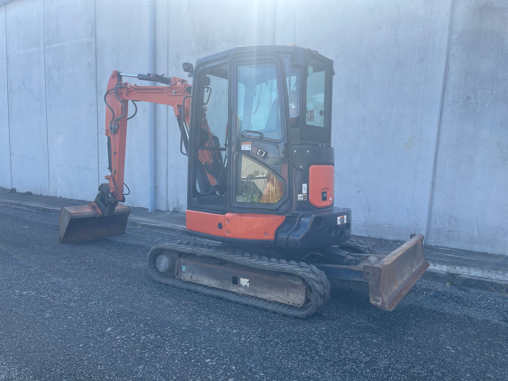A small orange excavator is parked in front of a concrete wall.