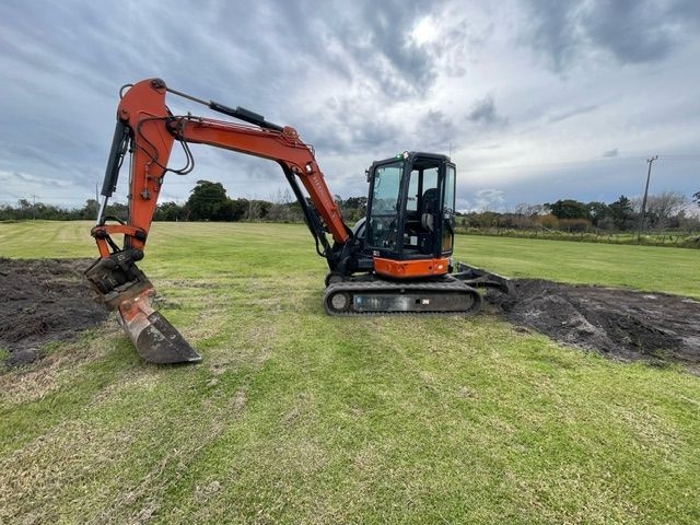 A small excavator is sitting in the middle of a grassy field.