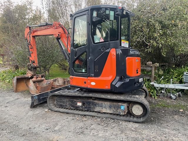 A small orange and black excavator is parked in a dirt lot.