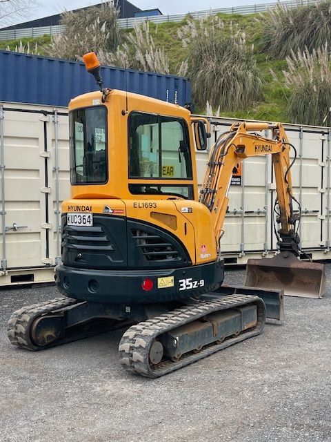 A yellow excavator is parked in front of a blue container.