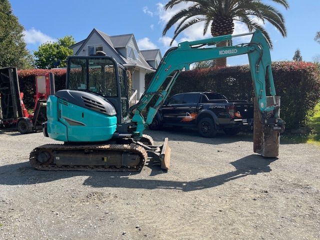 A small excavator is parked in a parking lot in front of a house.