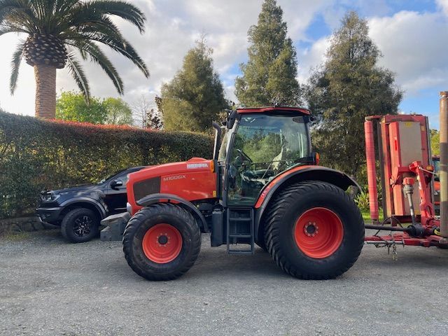 A red tractor is parked in a parking lot next to a palm tree.