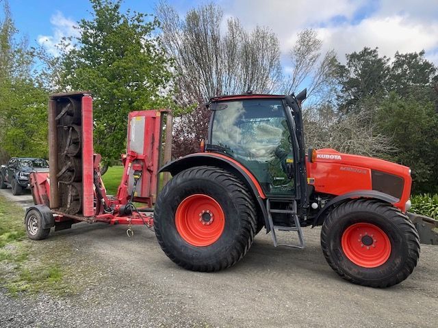 A red tractor is pulling a trailer with a mower attached to it.