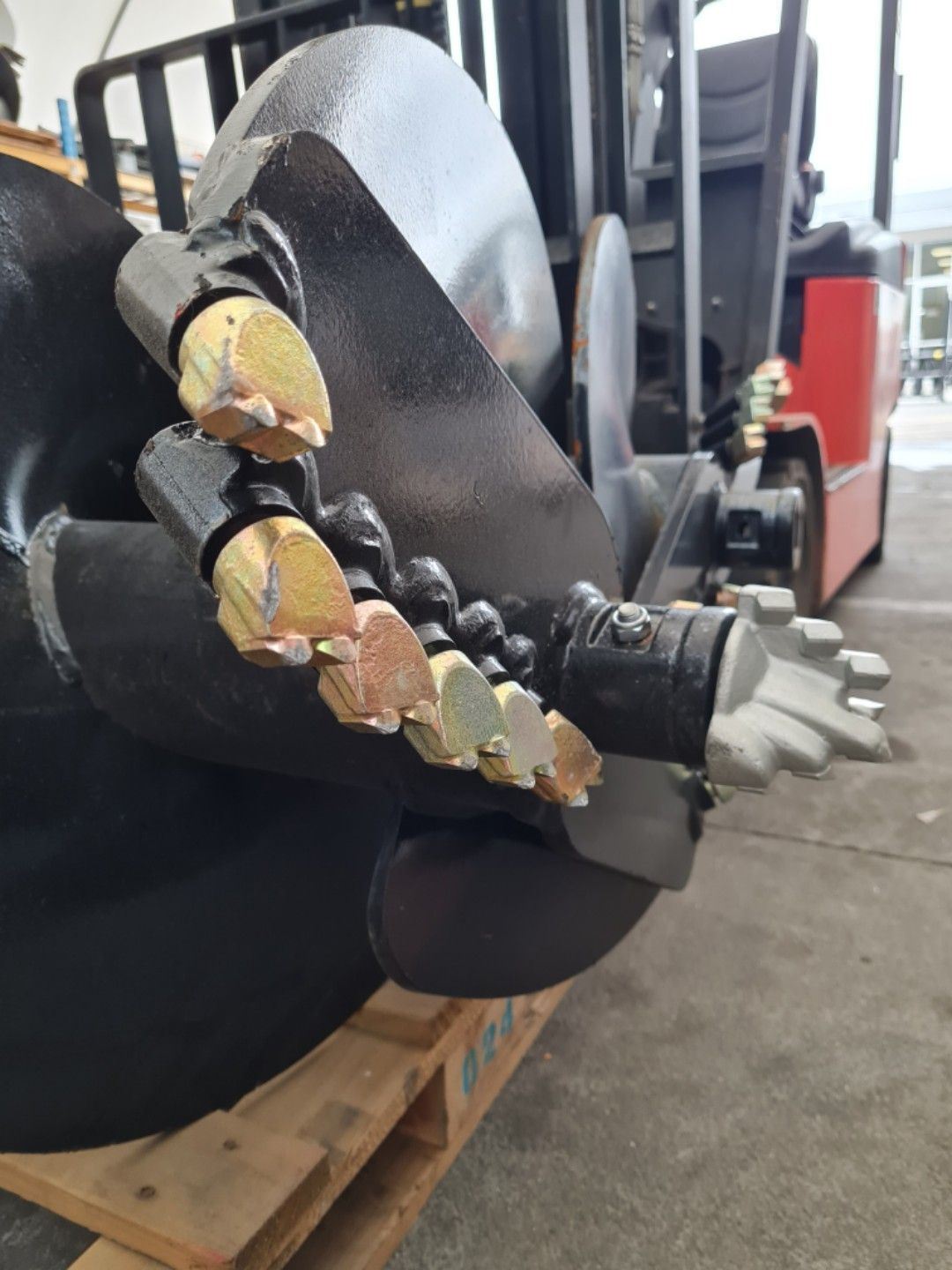 A large drill bit is sitting on a wooden pallet next to a forklift.