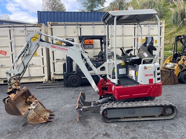 A small excavator is parked in a parking lot next to a forklift.