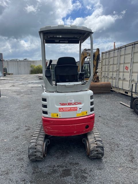 A small red and white excavator is parked in a parking lot.