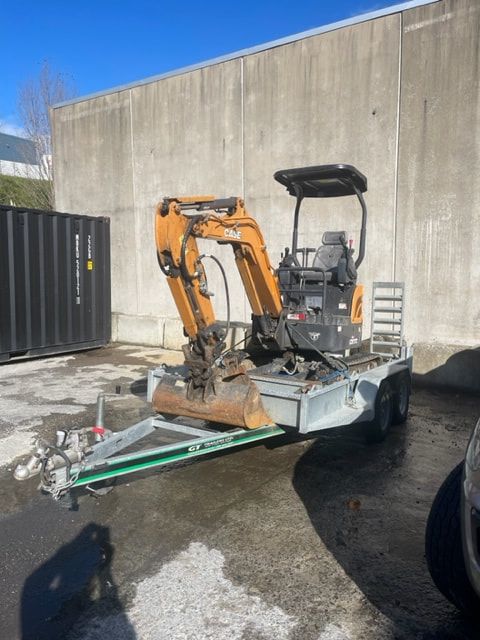 A small excavator is on a trailer in a parking lot