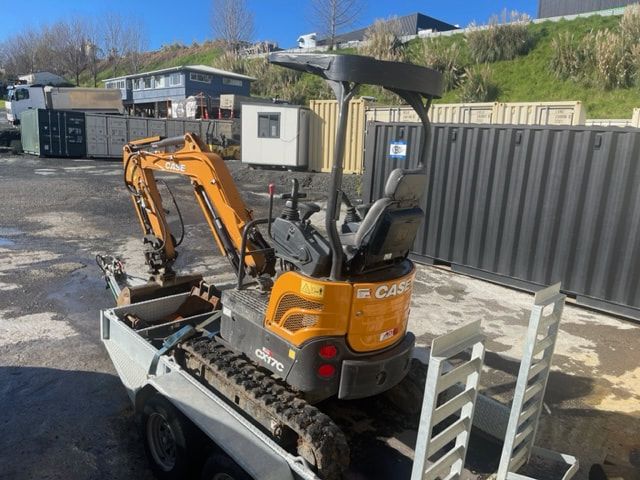 A small excavator is parked on a trailer in a parking lot.