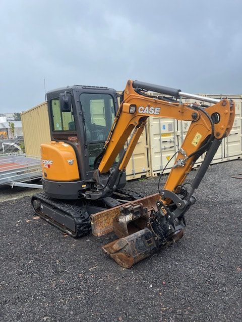 A small excavator is parked in a gravel lot next to a container.