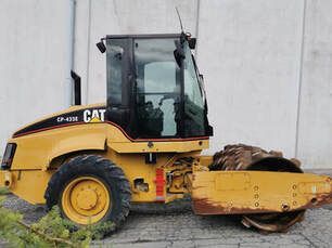 A yellow cat road roller is parked in front of a building.