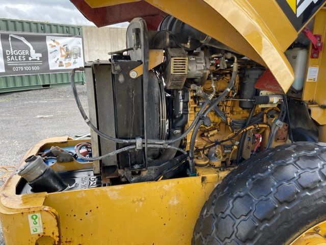 A yellow tractor with the hood up and a digger sales sign in the background
