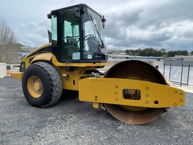 A yellow and black roller is parked in a gravel lot.