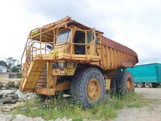 A large yellow dump truck is parked in a grassy field.