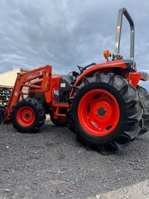 A red and black tractor is parked on a gravel road