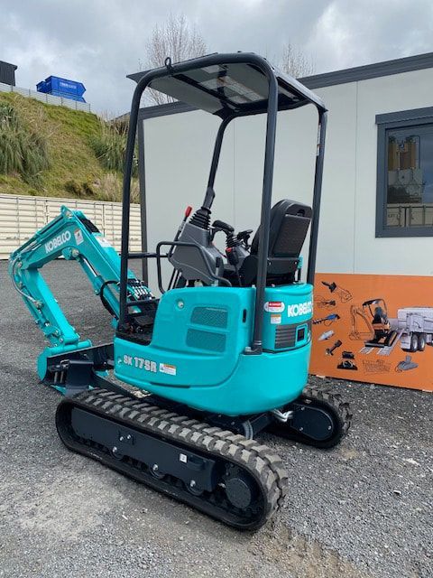 A small blue excavator is parked in front of a building.
