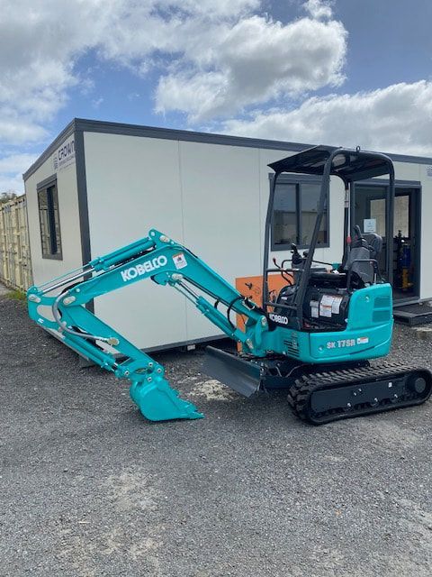 A small blue excavator is parked in front of a building.